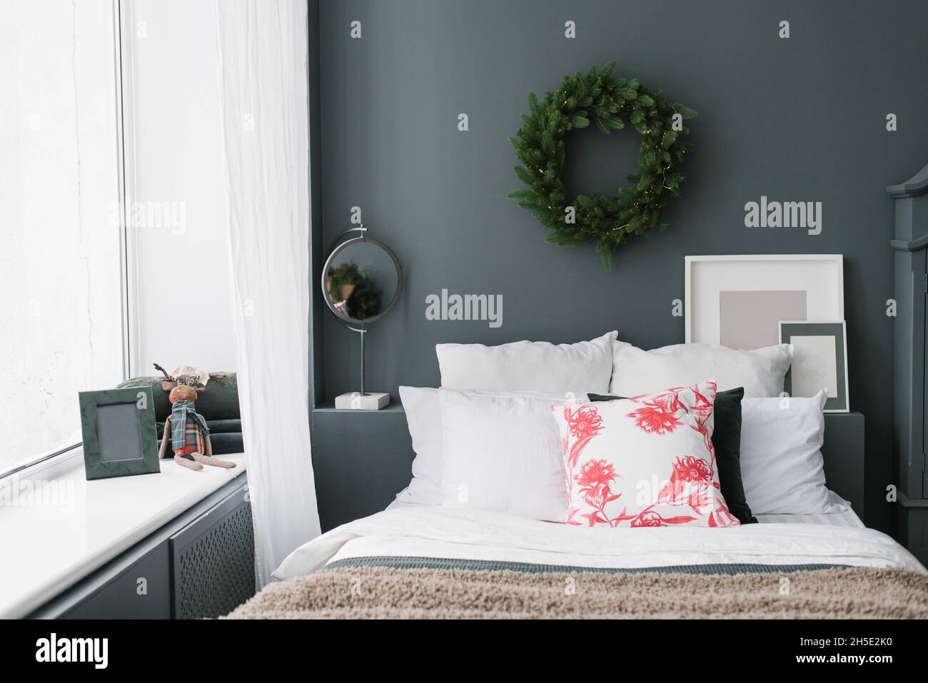 Elegante camera da letto di Natale. Cuscini sul letto e una corona sul muro Foto Stock