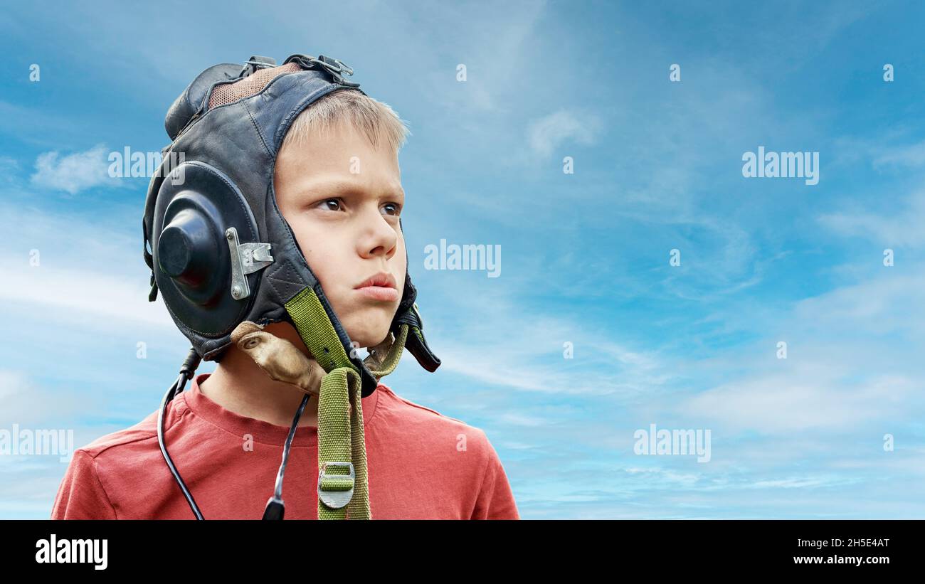 Ragazzo frustrato che indossa il casco pilota in pelle vintage guarda in alto nel cielo in piedi contro di cielo nuvoloso sfondo da vicino vista Foto Stock