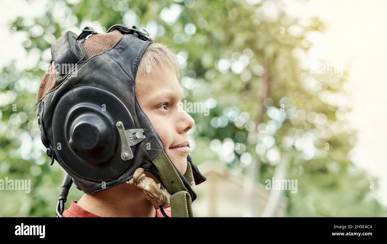 Vista del profilo di ragazzo adolescente positivo indossando casco pilota vintage in pelle in piedi nel parco verde in primavera giorno da vicino vista Foto Stock