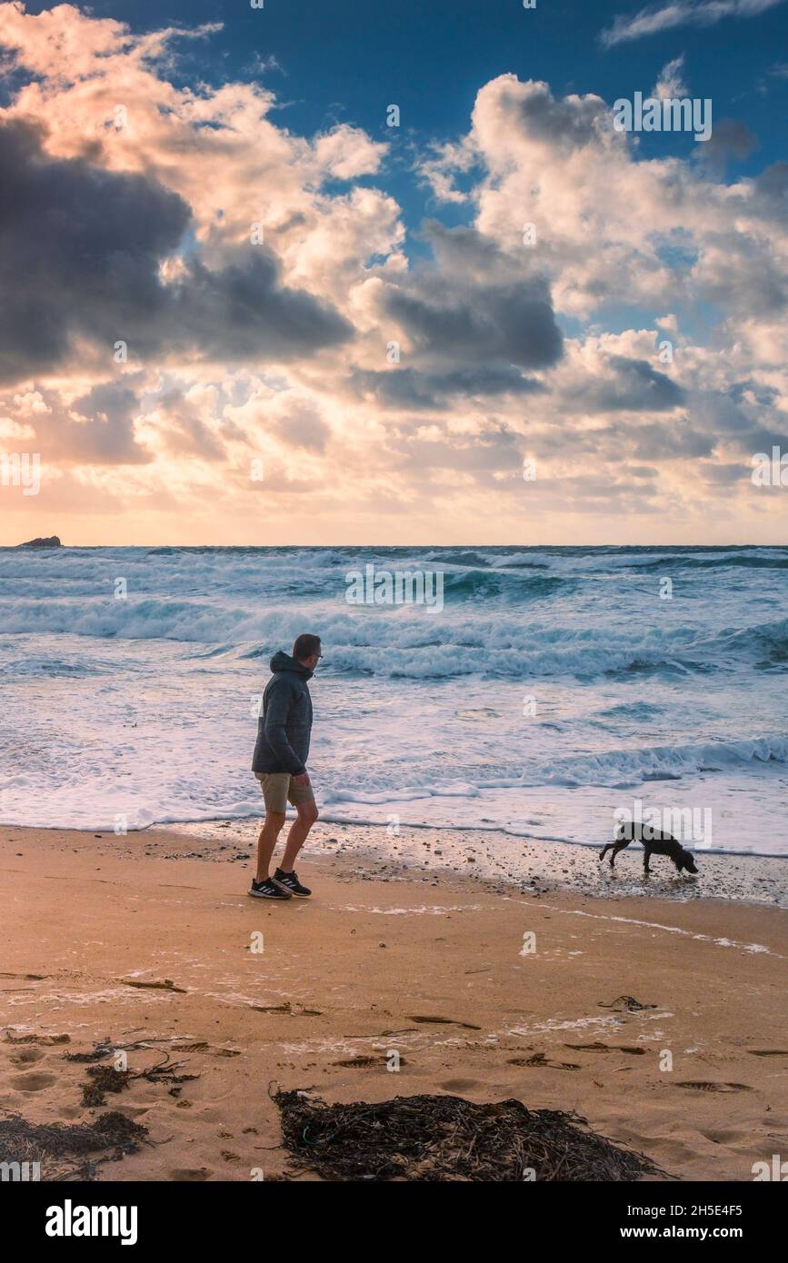 Sera luce su un uomo che cammina il suo cane lungo la costa su Fistral Beach a Newquay in Cornovaglia. Foto Stock
