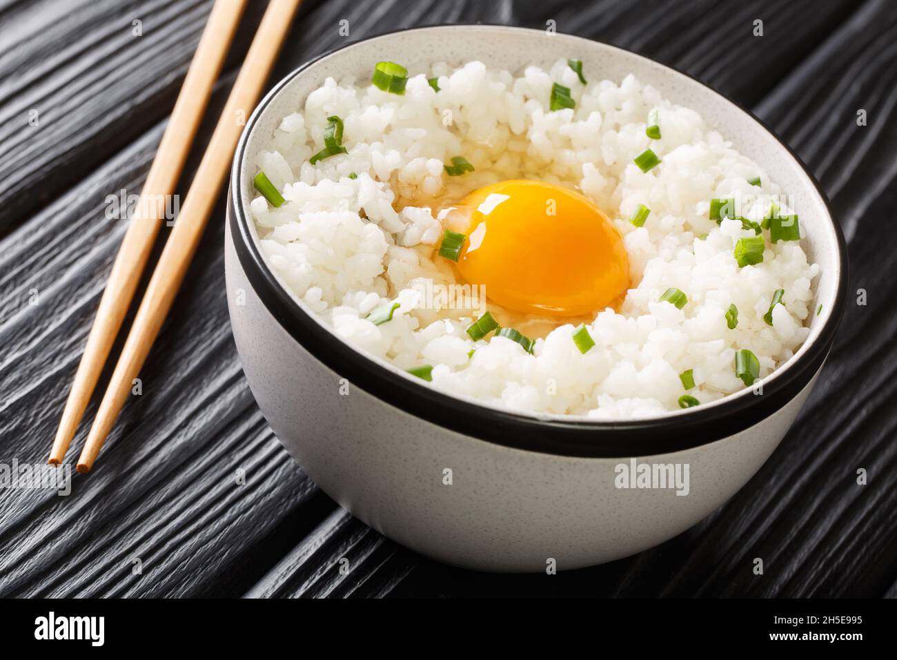 Tamago kake gohan è un piatto giapponese semplice fatto di uova crude su riso da vicino nella ciotola sul tavolo. Orizzontale Foto Stock