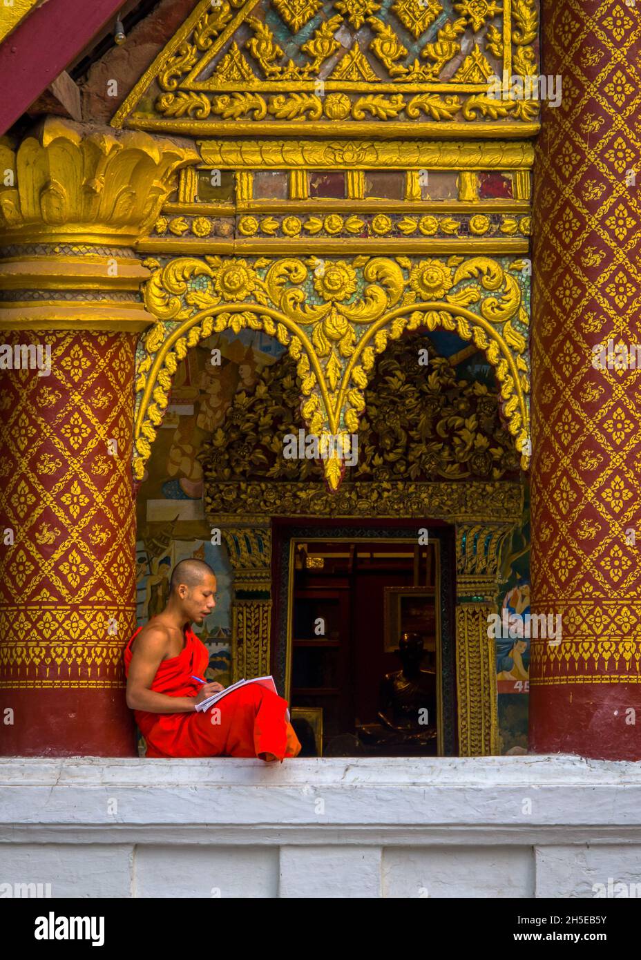 Luang Prabang, Laos - 4 febbraio 2018: Un giovane monaco si riposa contro una colonna decorata mentre studiava al Wat Xieng Mouane Foto Stock