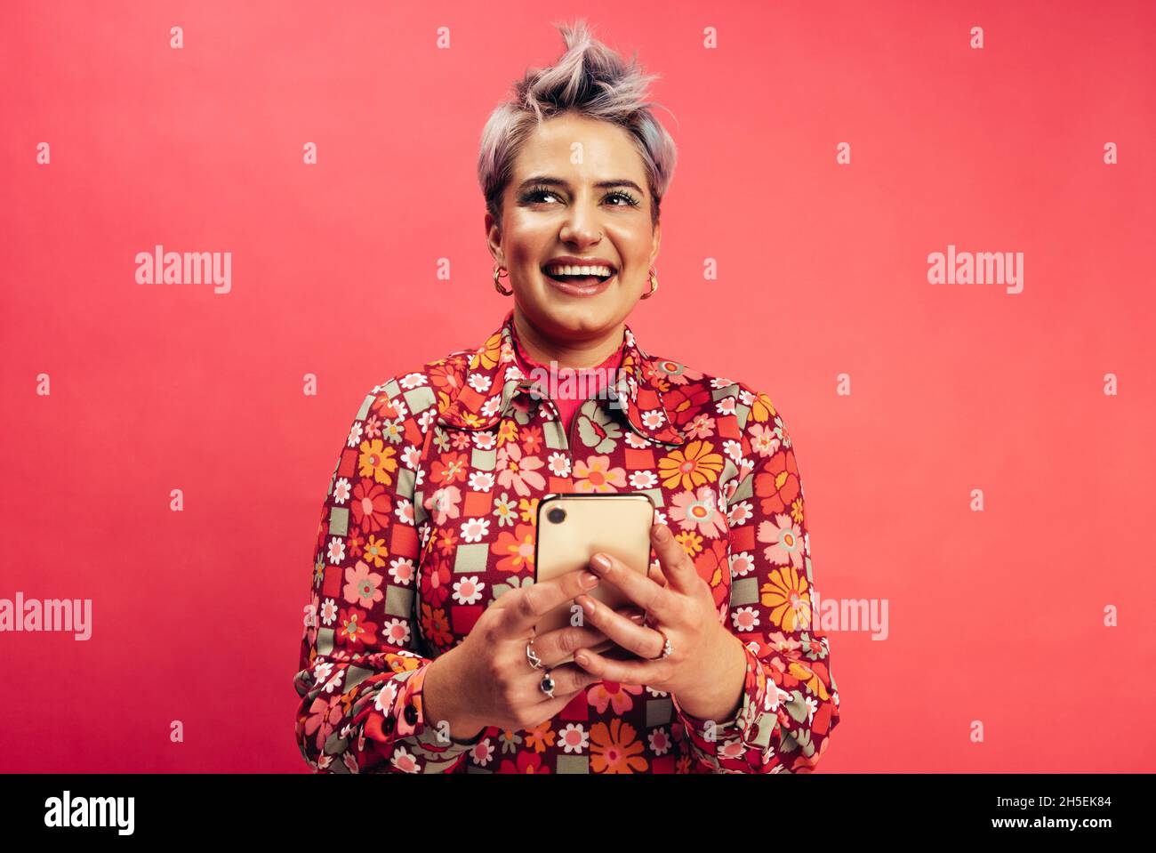 Giovane donna elegante con uno smartphone. Felice giovane donna sorridente allegro mentre navighi in internet in uno studio. Giovane donna con capelli tinti sta Foto Stock