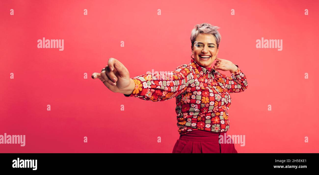 Ha ottenuto le mosse. Spensierate la giovane donna che balla e sorride allegramente mentre si alza su uno sfondo rosso. Giovane donna con capelli tinti con fu Foto Stock