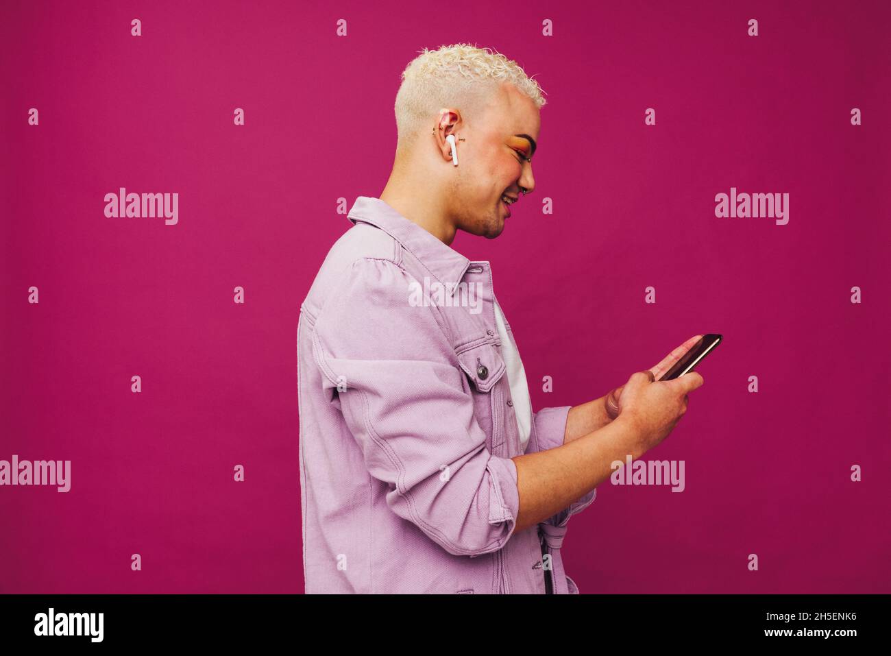 Giovane uomo alla moda che naviga tra le sue playlist musicali preferite. Felice uomo giovane che usa uno smartphone mentre indossa le cuffie wireless in uno studio. Non con Foto Stock