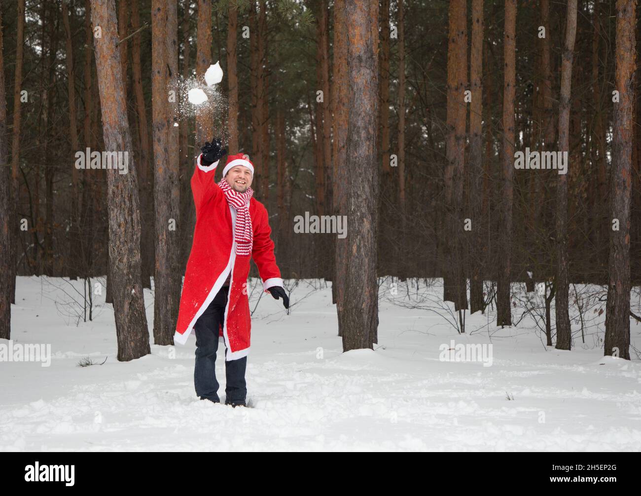 L'uomo allegro in una Santa Suit lancia palle di neve in una foresta nevosa. Vigilia di Natale, allegro inverno nevoso. In attesa di un miracolo, gioie invernali Foto Stock