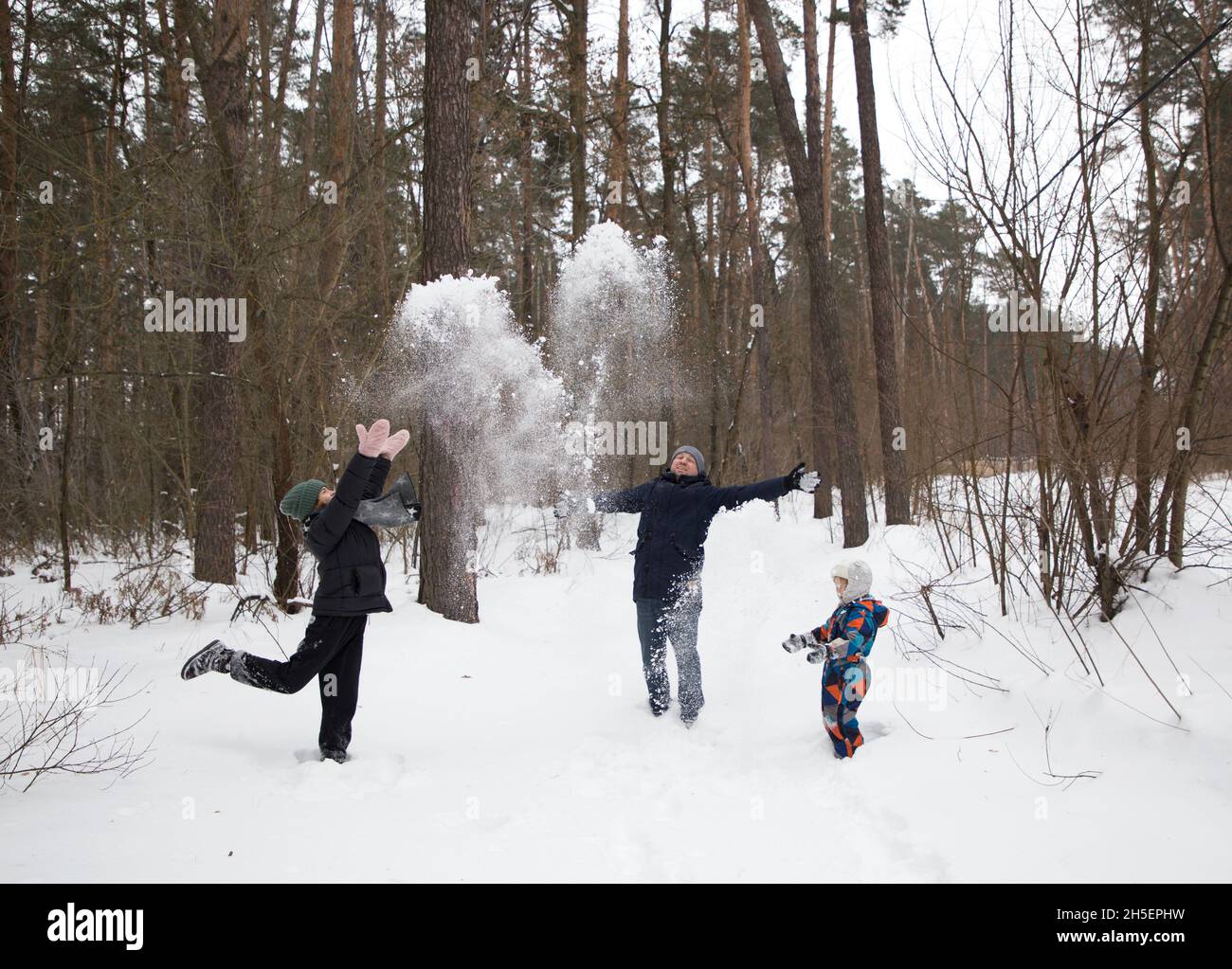 Divertimento invernale passatempo. Tre persone felici, uomo, donna, bambino, in abiti caldi che giocano all'aperto in inverno nel parco. Gettare sciolto soffice neve. Ciao wint Foto Stock