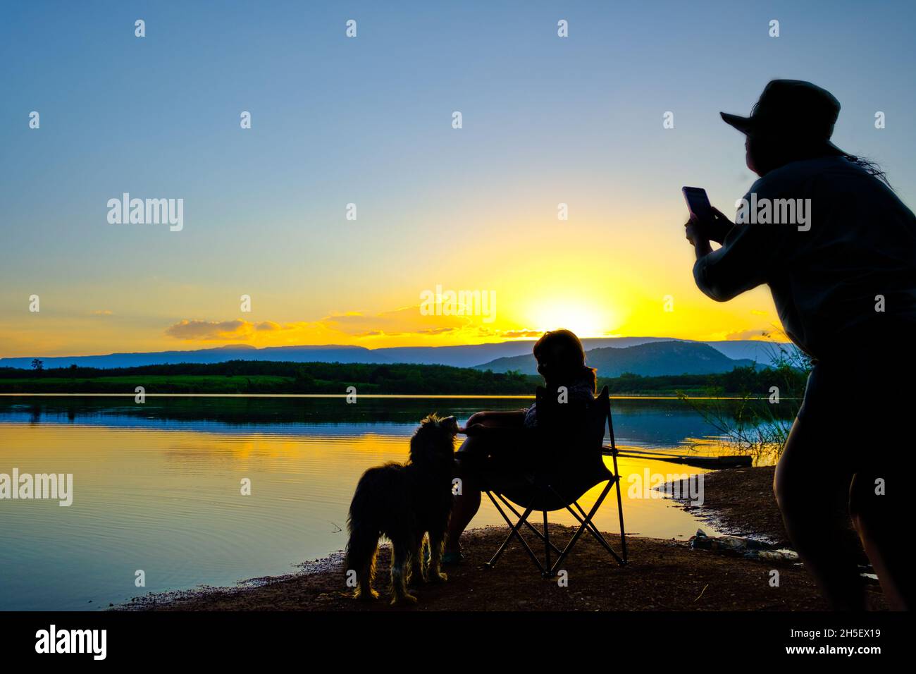 Silhouette di due giovani donne che scattano una foto su sfondo grigio sul lago al tramonto Foto Stock