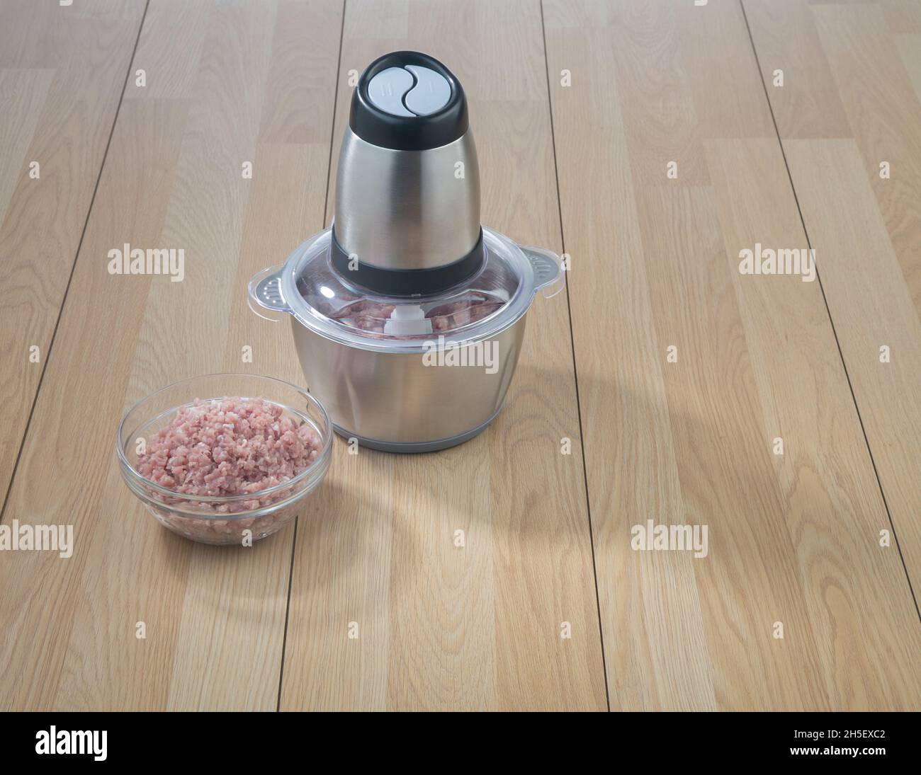 Robot da cucina con carne di maiale trita in una ciotola di vetro su sfondo tavolo di legno Foto Stock