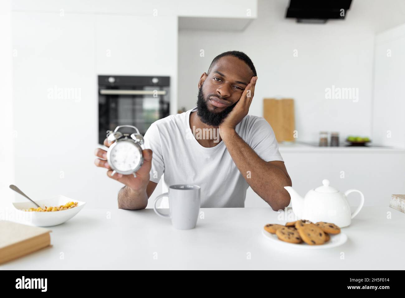 Uomo nero che soffre di insonnia che tiene mostrando sveglia Foto Stock