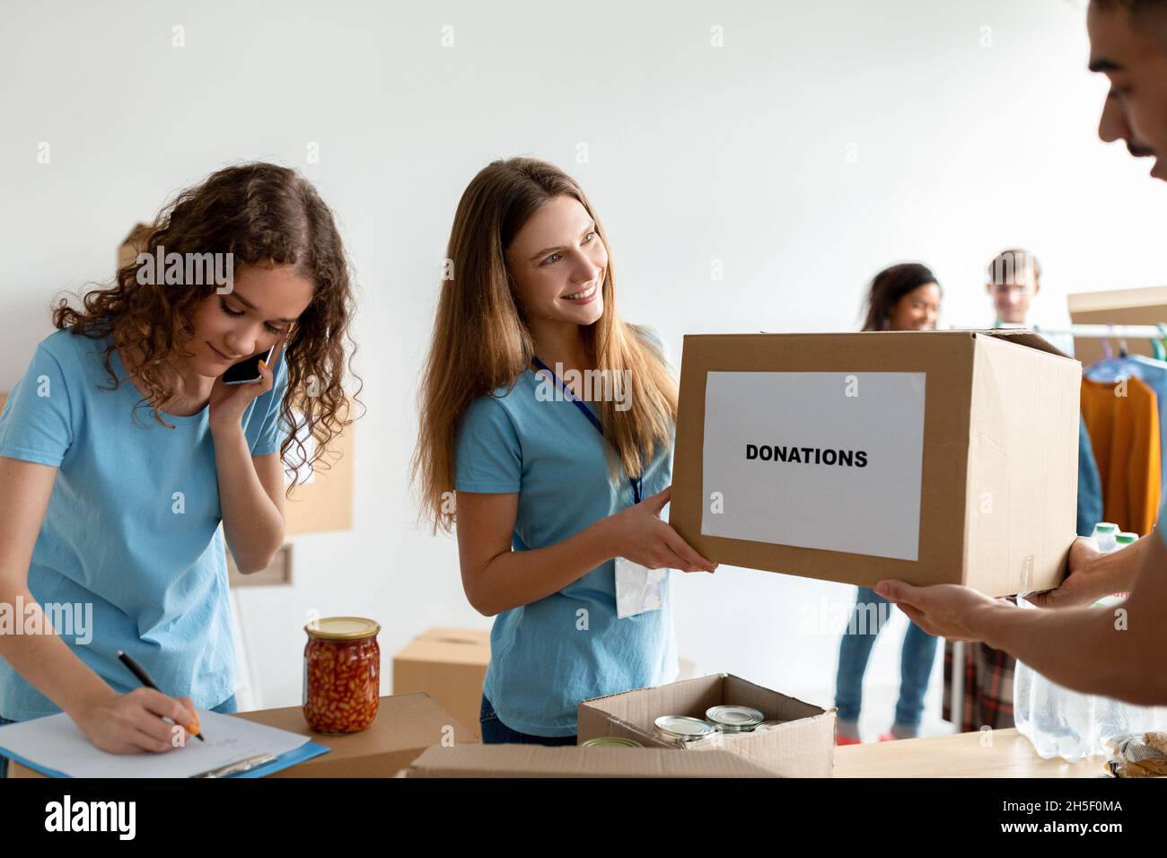 Volontariato. Uomo che dà scatola di cartone con donazioni a donna, assistente sociale che fa note negli appunti Foto Stock