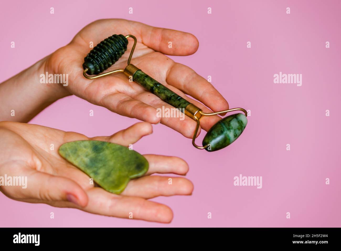 Jade Roller e scruber per massaggio viso in mani femminili su sfondo rosa. Foto Stock