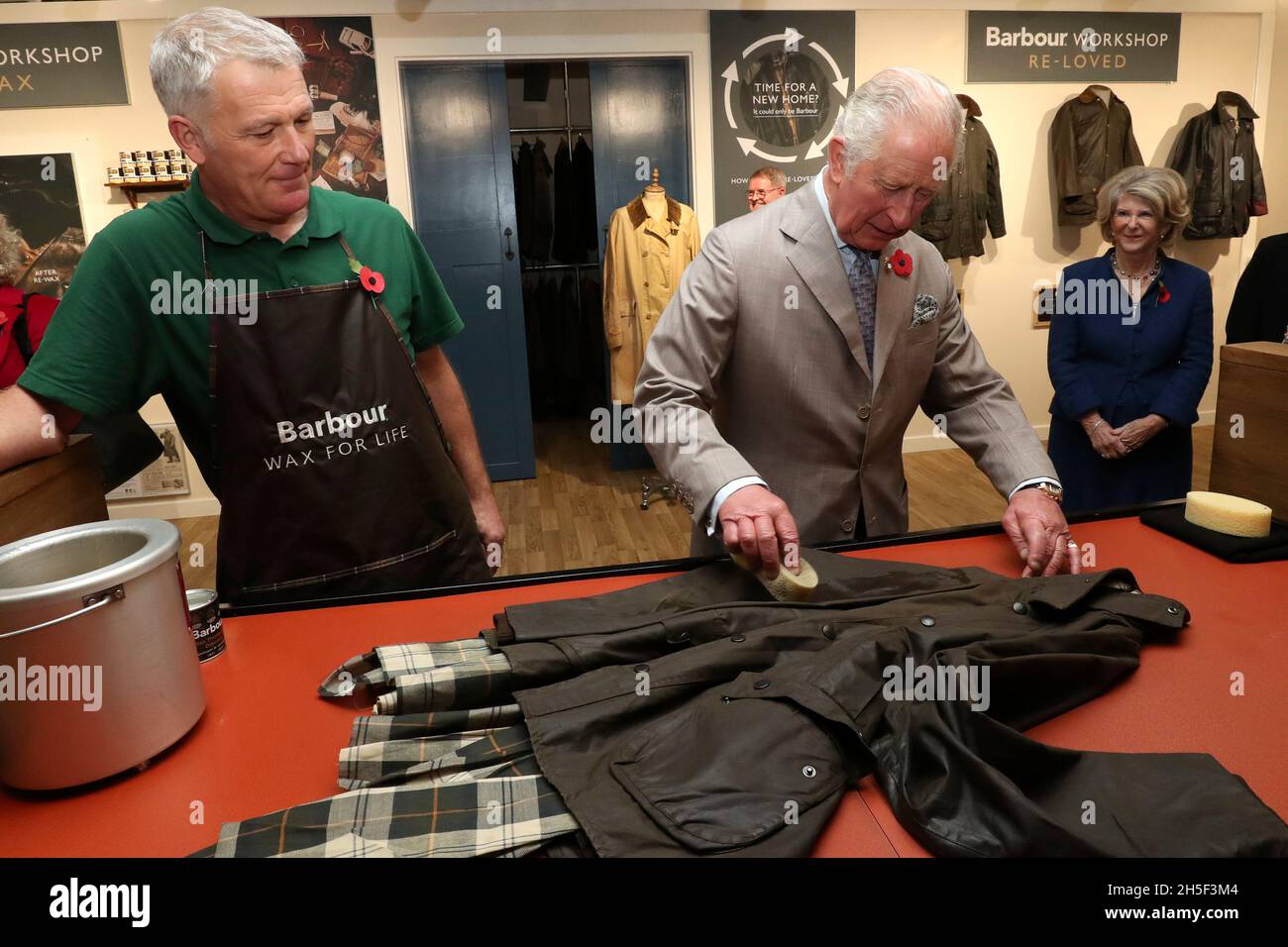 Neil Travis (a sinistra) guarda come il Principe del Galles cerca di rifare una giacca di cera durante il suo tour di J Barbour and Sons Ltd a South Shields, per segnare 100 anni di sostenibilità, durante una visita a Tyne and Wear. Data foto: Martedì 9 novembre 2021. Foto Stock