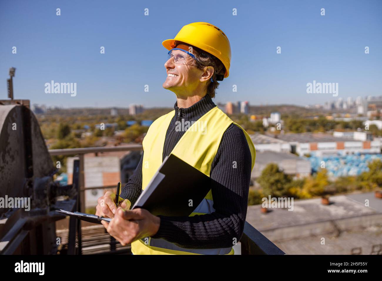 Gioioso ingegnere maschile con documenti in piedi all'aperto in fabbrica Foto Stock
