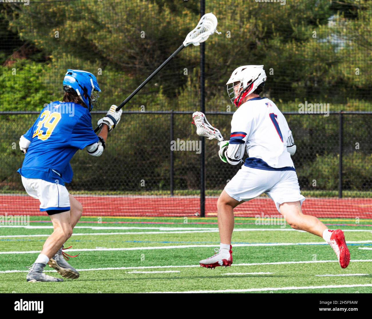 Un giocatore di lacrosse del ragazzo della scuola superiore che corre con la sfera sull'attacco come un difensore con un bastone lungo sta provando a arrestarlo durante una partita. Foto Stock