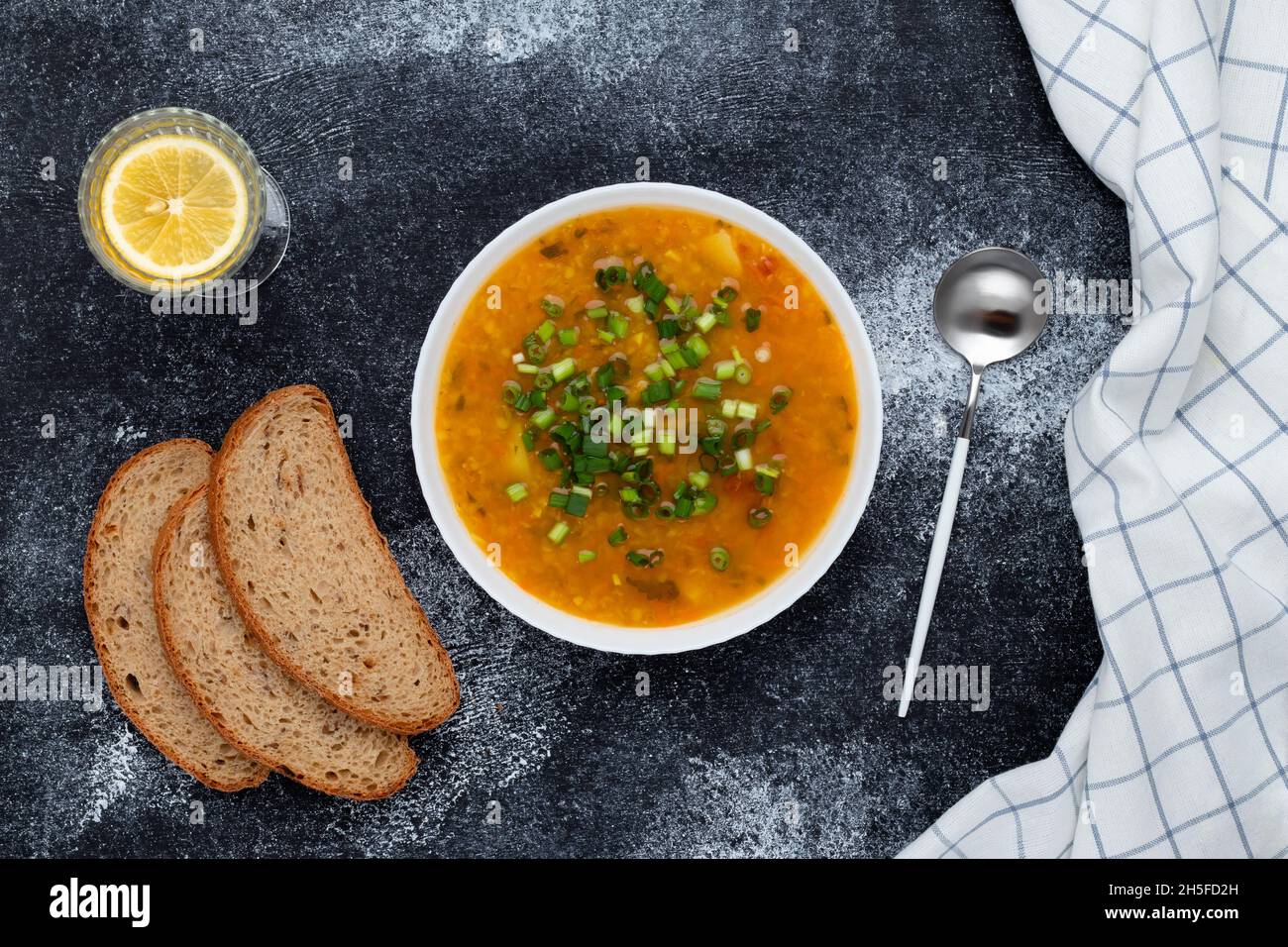 Una ciotola di zuppa di lenticchie rosse con pane sul tavolo nero. Vista dall'alto. Sfondo di cibo scuro. Un piatto di cucina greca tradizionale Foto Stock