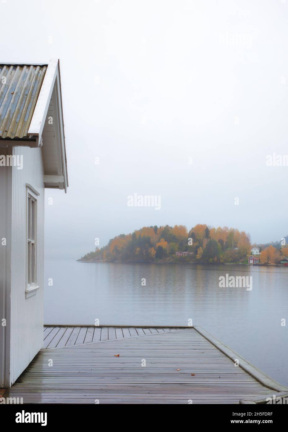 Cabina bianca d'epoca sulla costa del mare con molo bagnato. Colori oro fogliame. Piovoso, giorno di nebbia. Sfondo sfocato. Norvegia meridionale Foto Stock