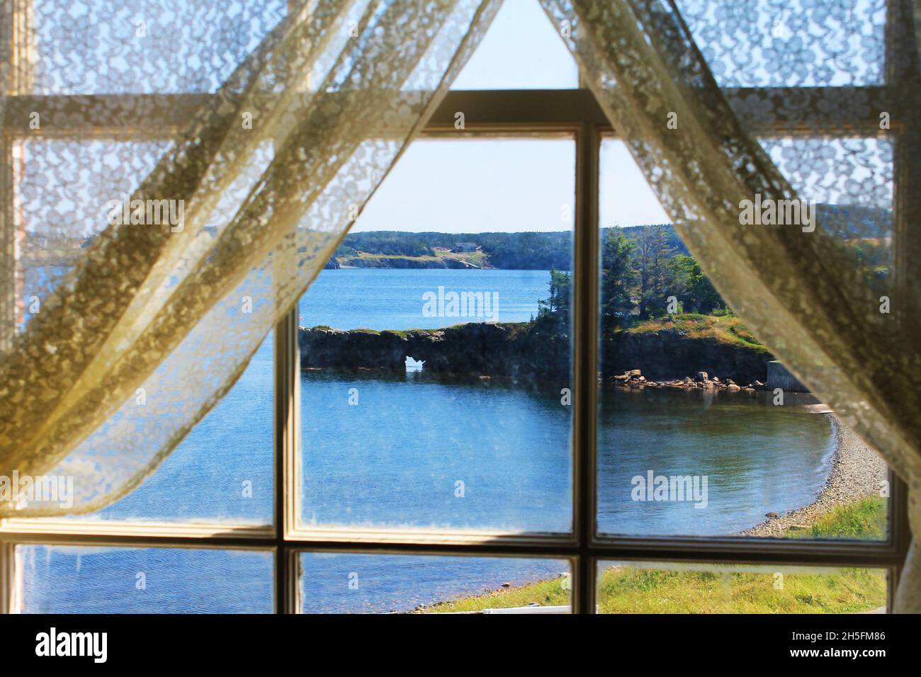 Vista della baia di Trinity, Terranova, attraverso una vecchia finestra incorniciata in legno, tende tirate indietro. Foto Stock