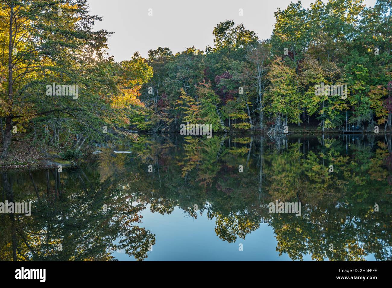 Pittoresco scenario di alberi luminosi e colorati che si specchiano nella quiete del lago mentre il sole sta scendendo evidenziando le cime degli alberi in Foto Stock