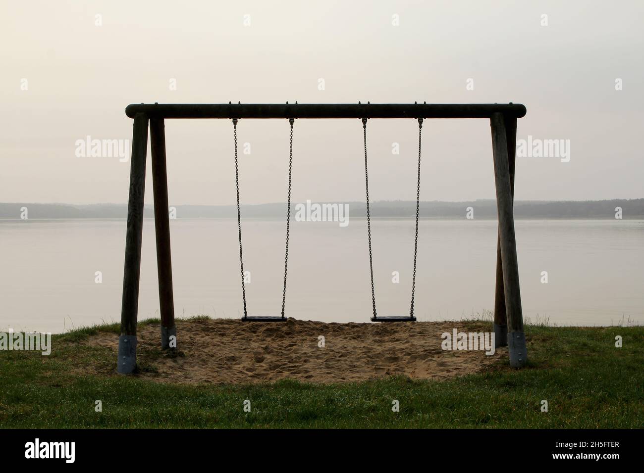 Eine leere Schaukel mit Blick auf einen leeren, dunstigen SEE. Foto Stock