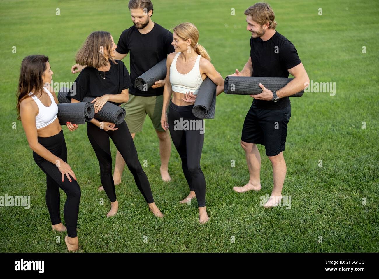 Le persone con materassini per il fitness si trovano in un prato verde Foto Stock