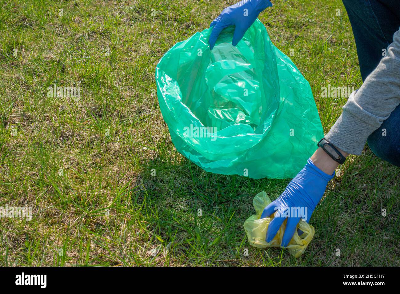 Donna che pulisce la natura di spazzatura. Fare volontariato con i guanti blu raccogliendo i rifiuti in un sacchetto di plastica. Volontariato, inquinamento, ecologia e plastica Foto Stock