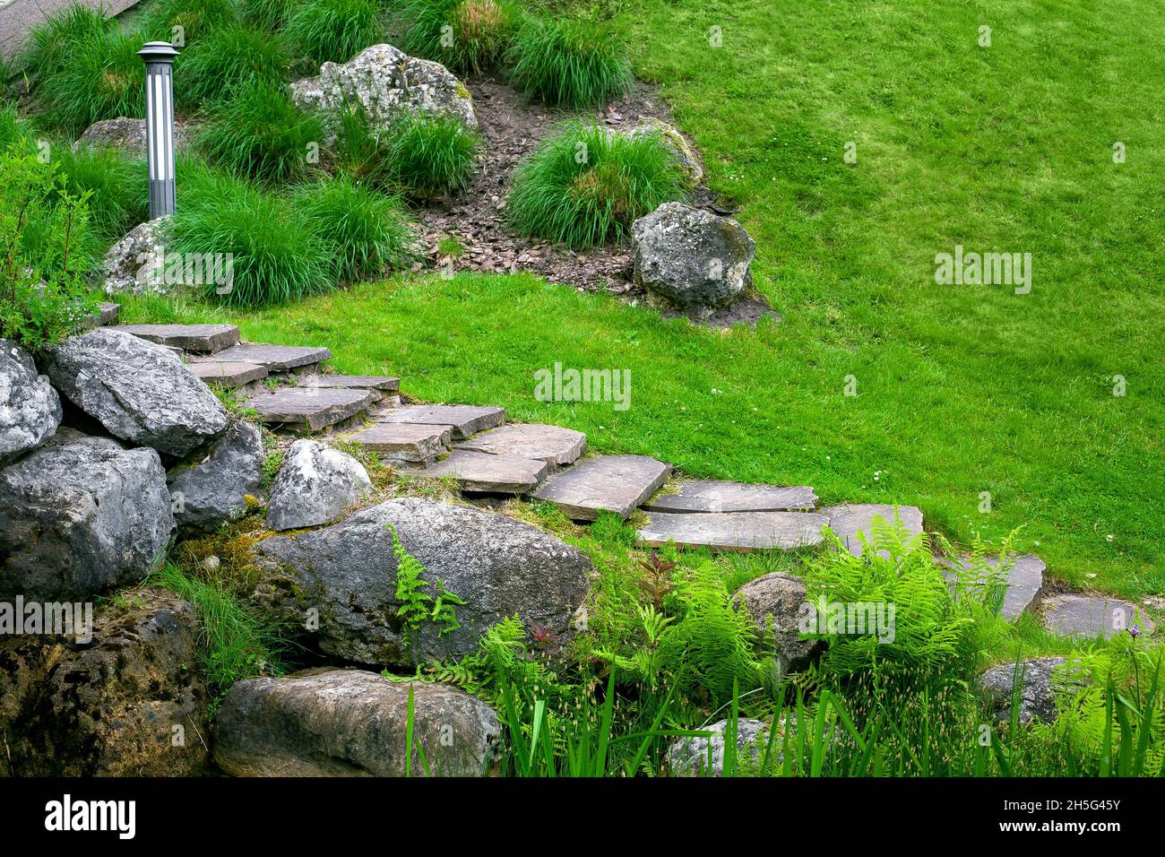scala in pietra con scalini in pietra naturale selvaggia sul pendio del parco collinare paesaggio con roccia, terreno giardino lanterna tra piante verdi in estate en Foto Stock