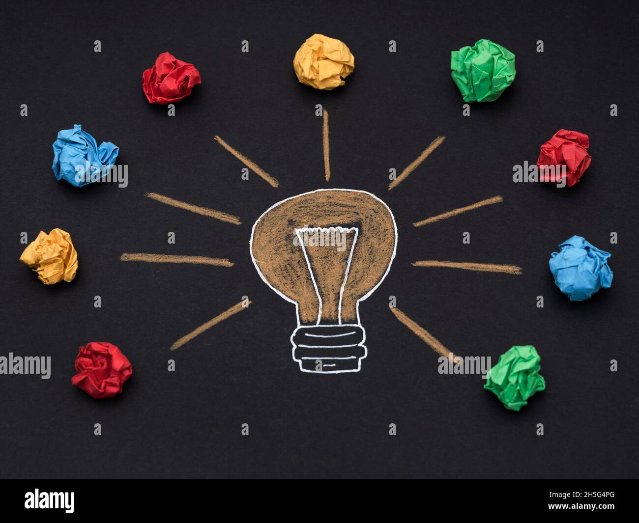Un disegno di una lampadina con colorate sfere di carta sgualcite intorno ad essa. Primo piano. Foto Stock