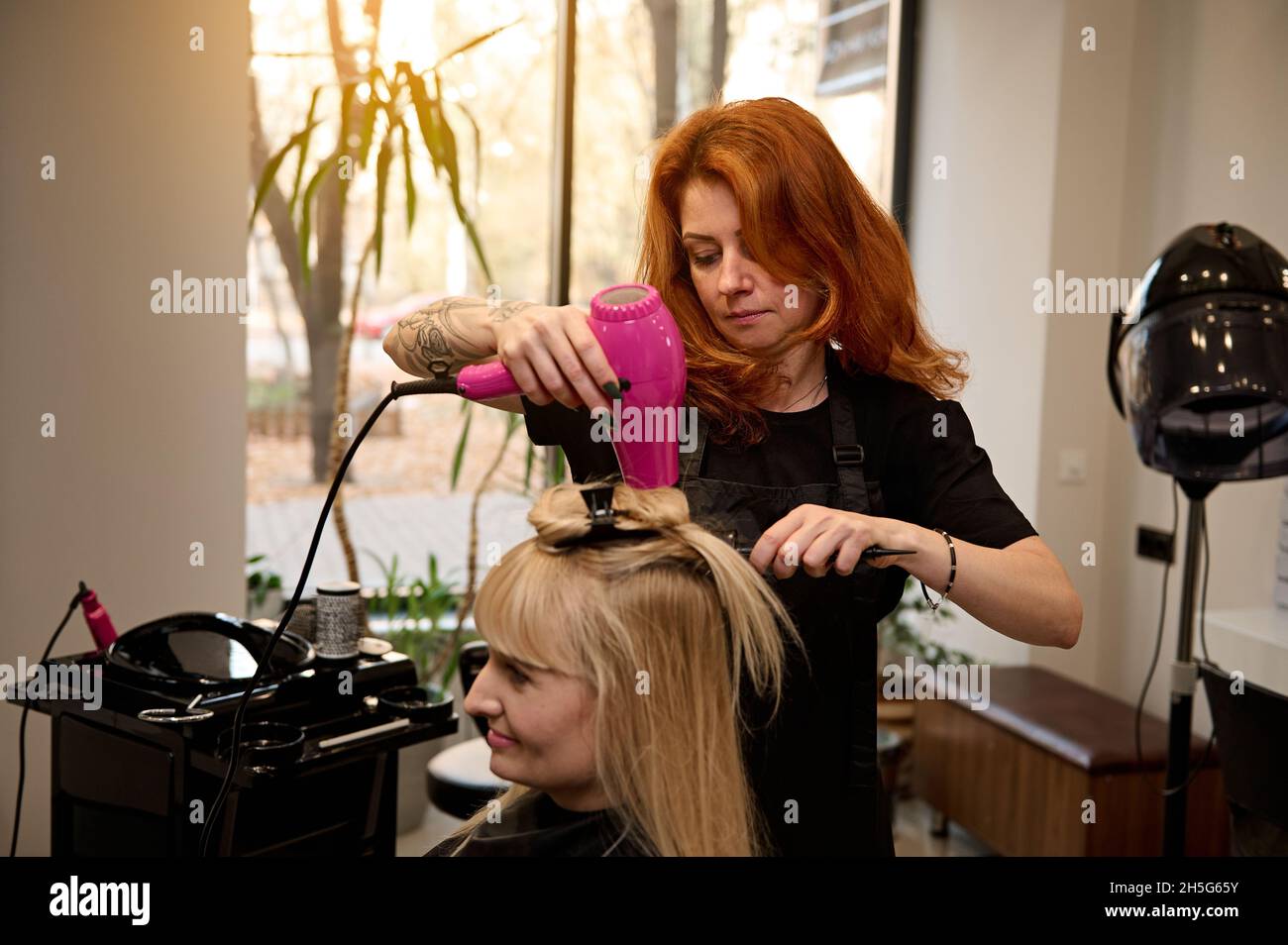 Parrucchieri professionale alla moda redhead con un pettine rotondo e  asciugacapelli raddrizza i capelli biondi ad un cliente di un salone di  bellezza, eseguendo un a Foto stock - Alamy