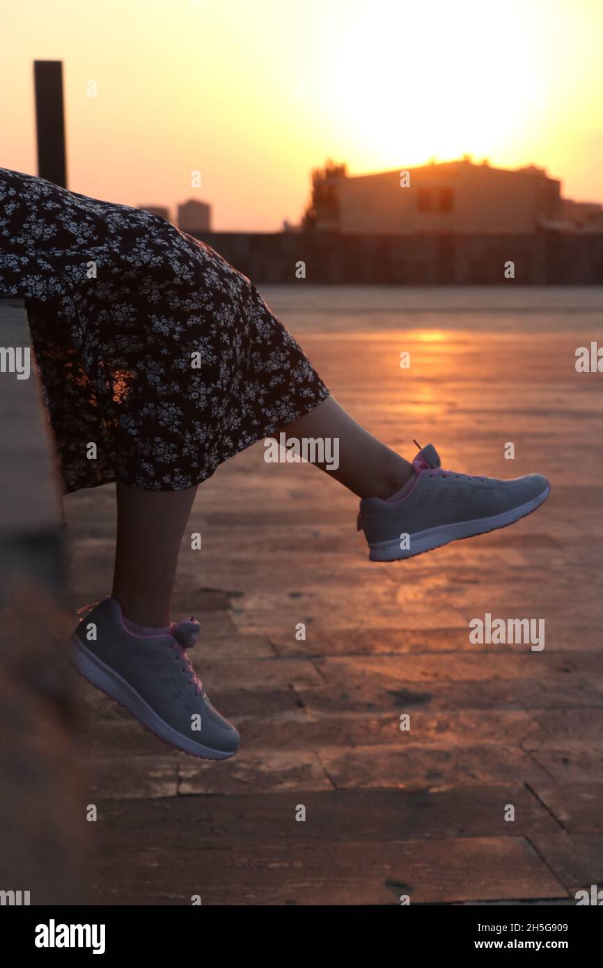 Scatto verticale di giovani piedi femminili all'aperto nelle scarpe sportive e abito nero con stampa a margherita Foto Stock