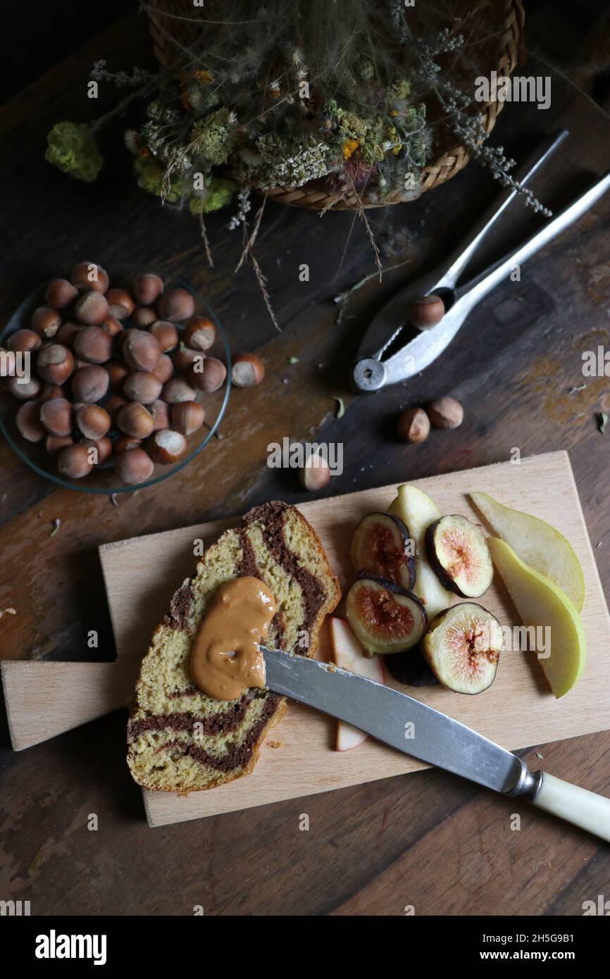 Vassoio di legno con torta di crema al cioccolato e fichi e pere affettati vicino a una ciotola di nocciole Foto Stock