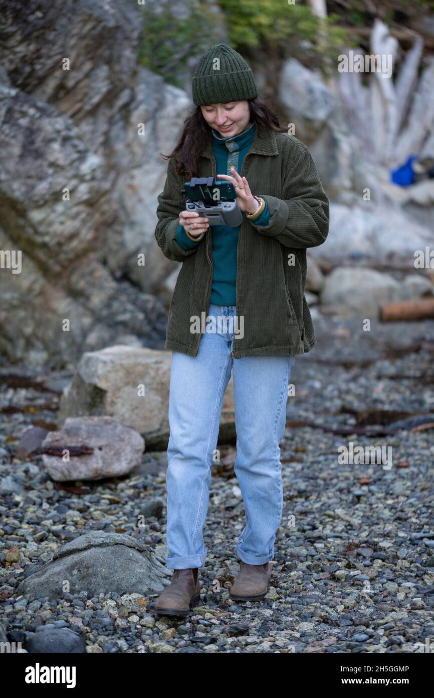 Giovane donna sta usando il telecomando per un drone in Whytecliff Park, Horseshoe Bay; British Columbia, Canada Foto Stock