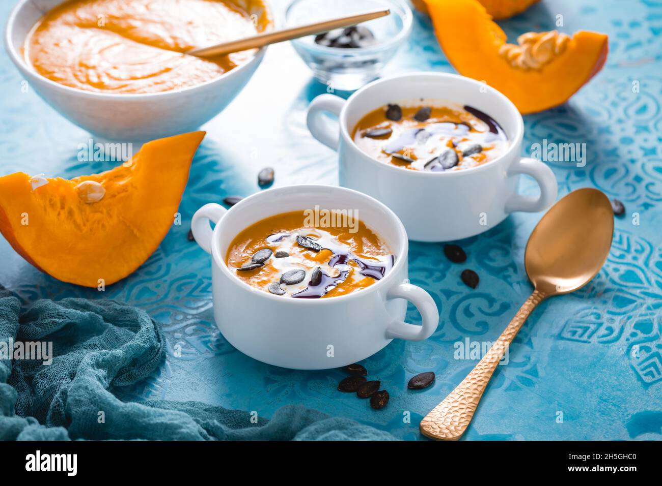 Zuppa di zucca fatta in casa con latte di cocco, olio di zucca e semi su sfondo blu Foto Stock
