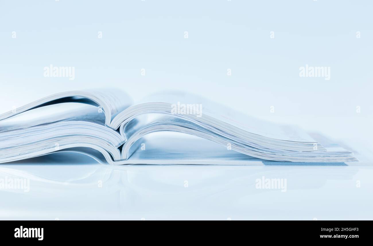 Pila di riviste aperte con tono blu su sfondo bianco e spazio per la copia Foto Stock