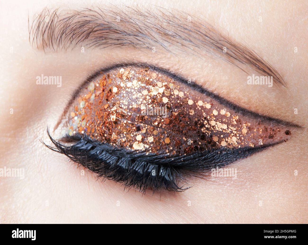Primo piano di faccia femminile con Vogue dorate lucenti occhi trucco. Occhio chiuso. Foto Stock