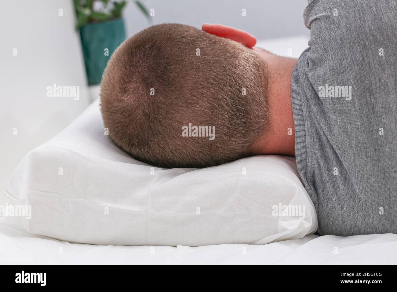 L'uomo dorme su uno speciale cuscino anatomico ortopedico per una schiena piatta e un sonno sano. Foto Stock