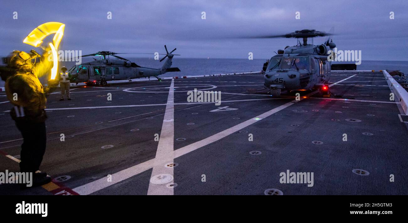 OCEANO PACIFICO (Nov. 6, 2021) Airman Kevon Lamont-Anderson di Aviation Boatswain, di Cleburn, Texas, assegnato alla nave portuale di trasporto anfibio USS John P. Murtha (LPD 26), Dirige un elicottero MH-60S Seahawk attaccato alle "Wild Cards" di Helicopter Sea Combat Squadron (HSC) 23 per salire dal ponte di volo durante il NASA in corso Test di recupero nove (URT-9), 6 novembre. Questo segna il nono test di recupero in corso della Marina degli Stati Uniti a sostegno della missione della NASA Artemis e la terza volta che un URT ha avuto luogo a bordo di John P. Murtha. La Marina degli Stati Uniti ha molte capacità uniche che la rendono un partner ideale f Foto Stock