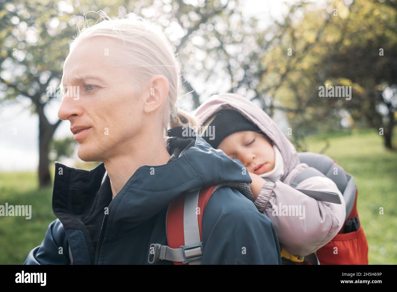 Uomo a piedi con bambino sonnolento in montagna. Bambino seduto in zaino sul retro del padre. Avventura attiva in famiglia nella foresta con ragazza stanca. Freddo Foto Stock