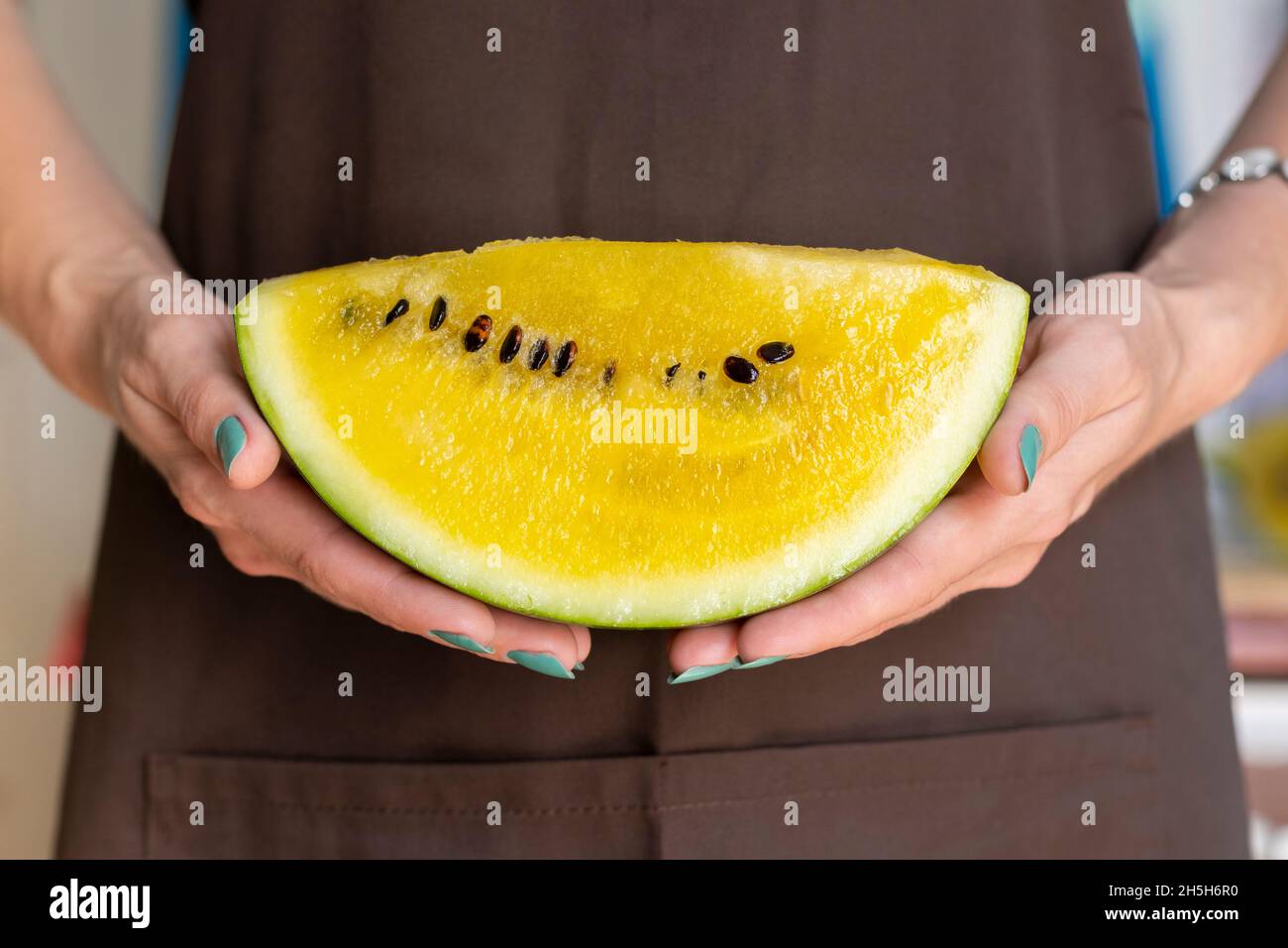 Le mani femminili di una donna stanno tenendo una parte tagliata di un anguria gialla. È il momento di assaggiare il melone giallo. Foto Stock