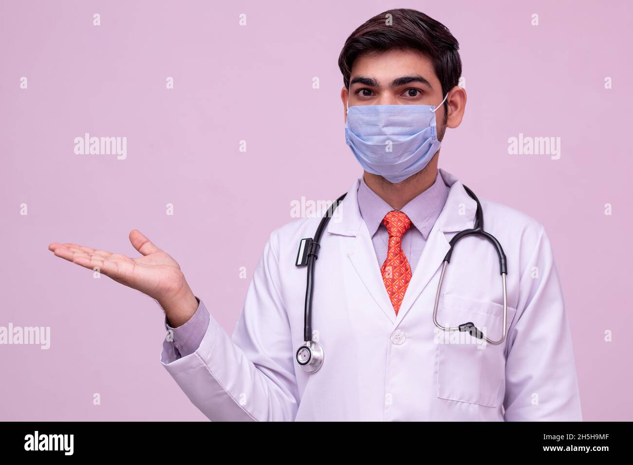 giovane medico indossare maschera che tiene qualcosa in mano vuota sfondo isolato. Foto Stock