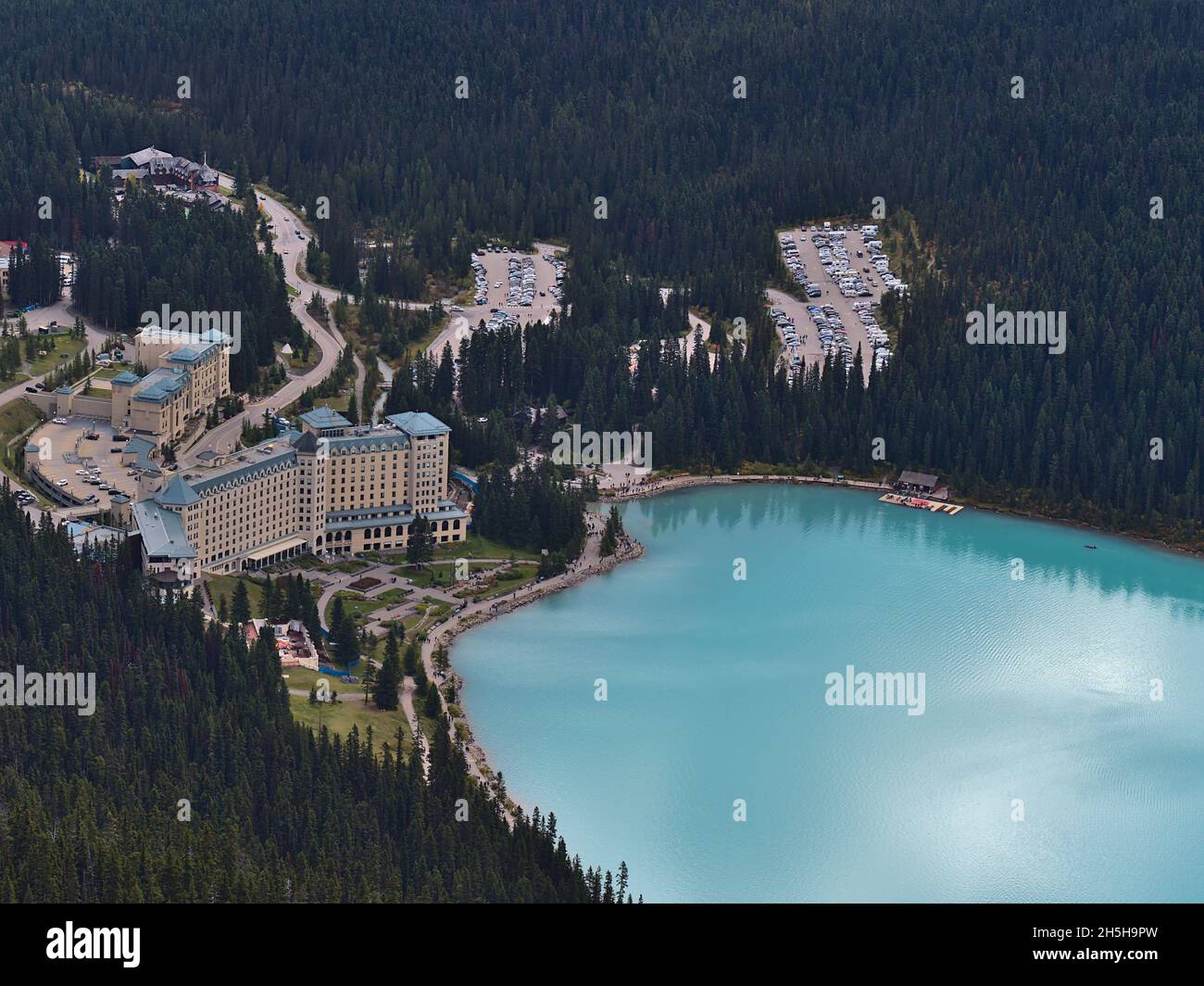 Vista ad alto angolo del Lago Louise orientale con acqua color turchese, famoso hotel e parcheggio auto circondato da foreste nel Parco Nazionale di Banff, Canada. Foto Stock