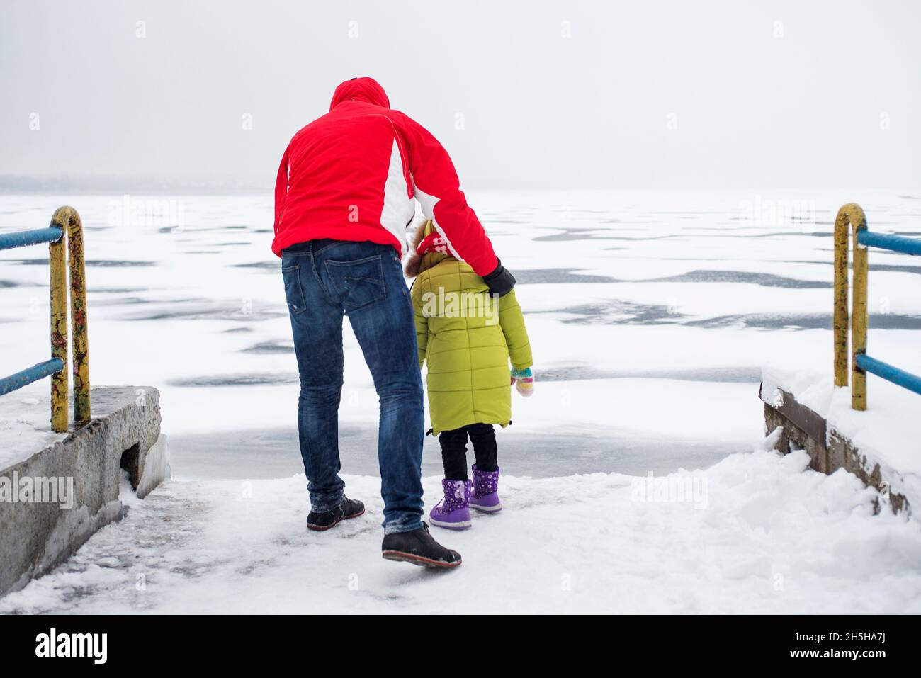 Un bambino con il padre cammina in prossimità di un lago ghiacciato o di un fiume Foto Stock
