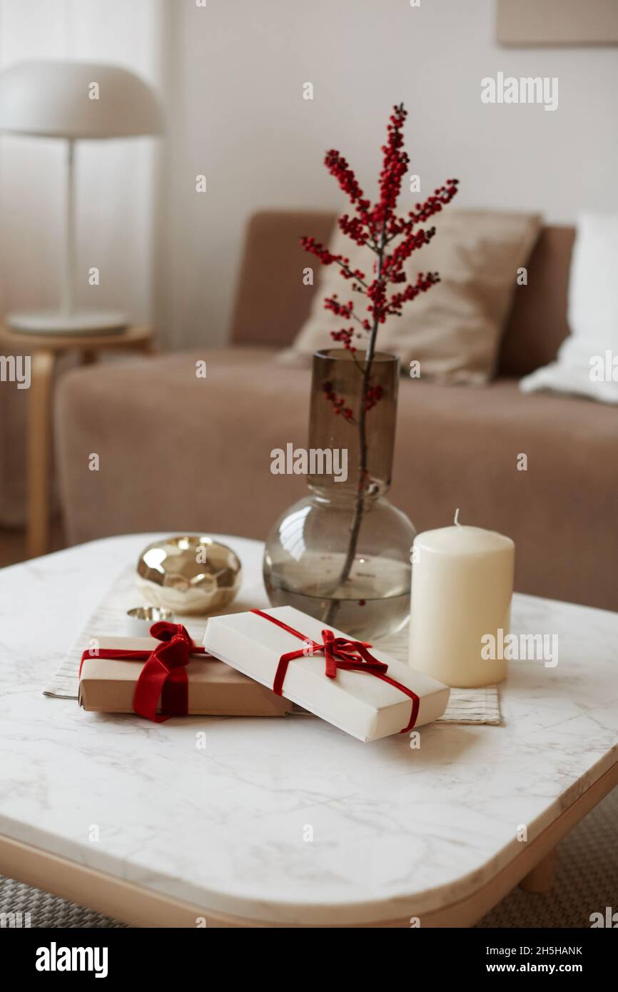 Scatola regalo di Natale con disegno minimalista della confezione, candela e vaso con una certa pianta sul tavolo bianco. Il concetto di eventi di celebrazione e. Foto Stock