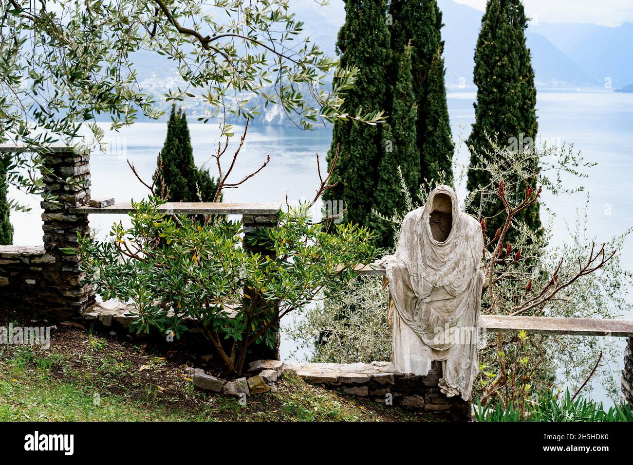 Statua fantasma su un recinto in pietra tra alberi verdi sulle rive del Lago di Como. Italia Foto Stock