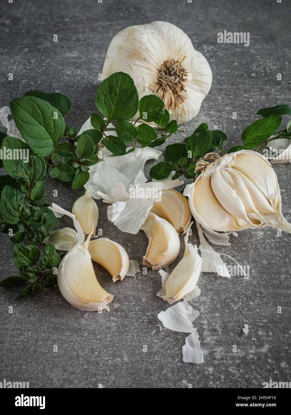 Bulbi di aglio (allio) e foglie di origano fresco su sfondo scuro. Spazio di copia. Foto Stock