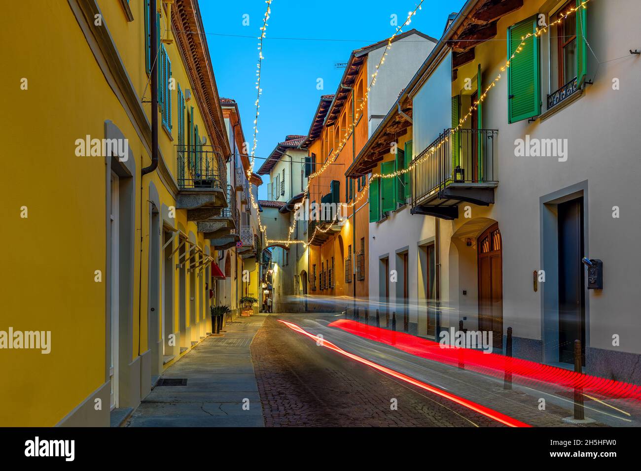 Strada stretta e vecchie case illuminate dalle luci di Natale in serata nel centro storico di Alba, Piemonte, Italia settentrionale. Foto Stock