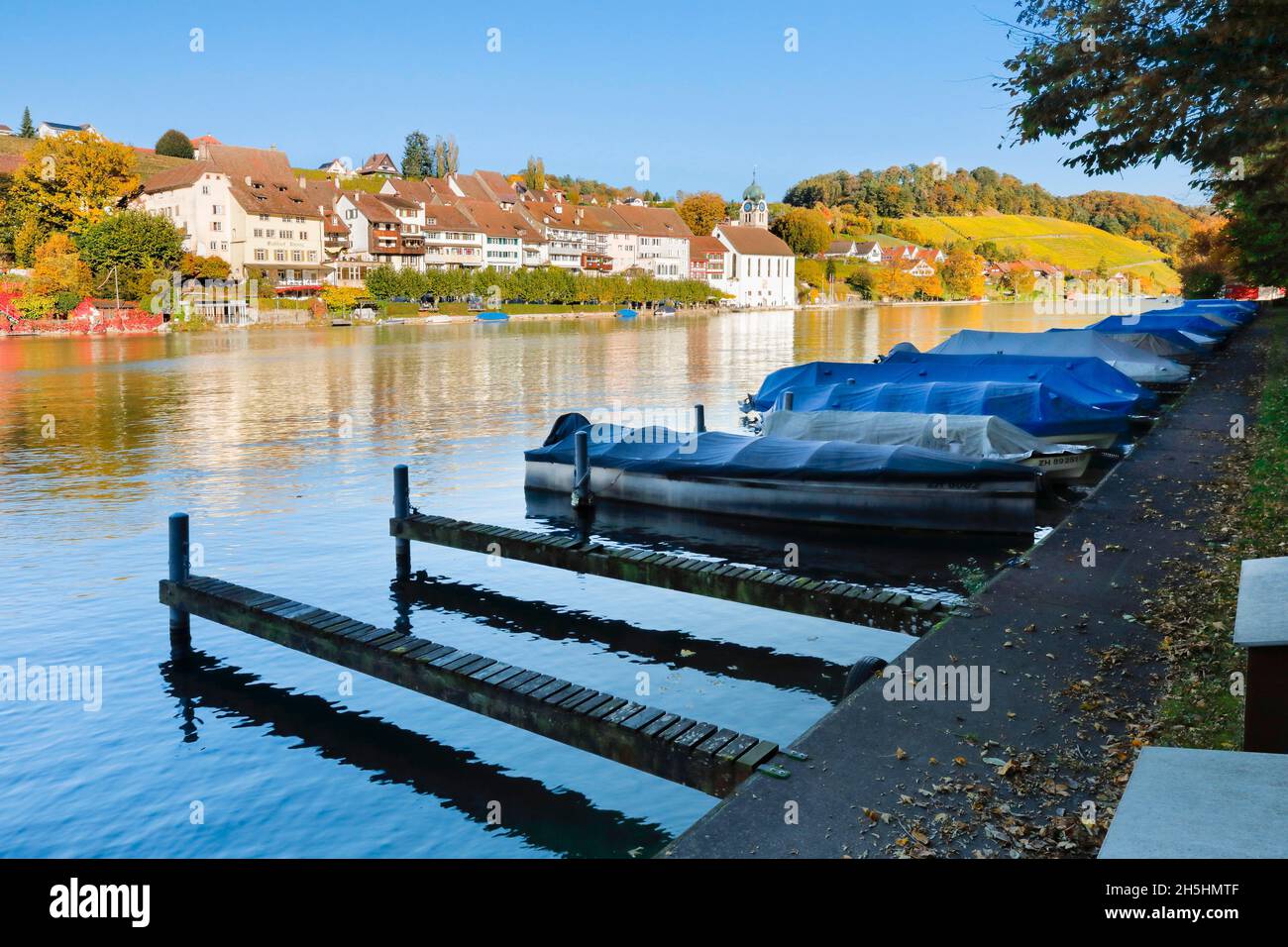 Vista dalle rive del Reno sul Reno verso la città vecchia di Eglisau con riflessione sull'acqua del fiume, barche scongelate con molo nel Foto Stock