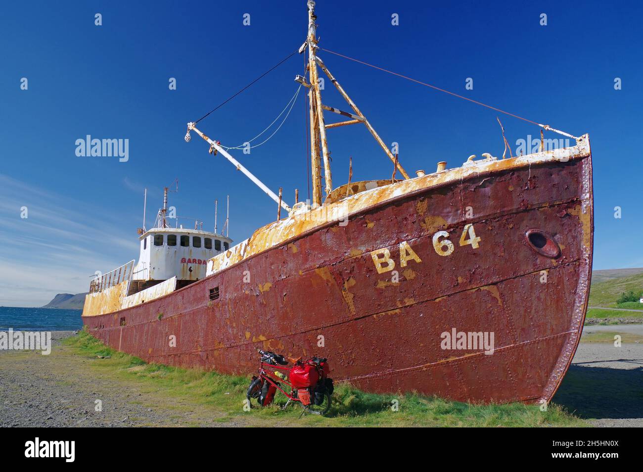 Vecchia barca da pesca situata sulla spiaggia, arrugginita, bicicletta di fronte ad essa, Patreksfjoerdur, Westfjords, Islanda Foto Stock