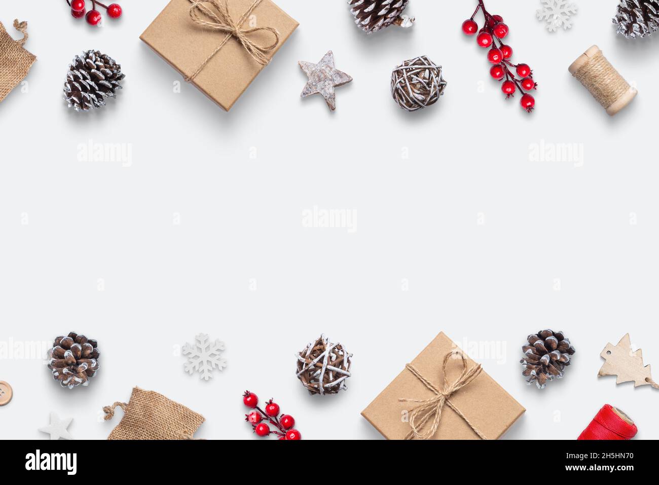Sfondo natalizio con regali rustici e decorazioni su superficie bianca. Coni di pino, rose, palle, alberi di legno, fiocchi di neve e stella. Vista dall'alto con c Foto Stock