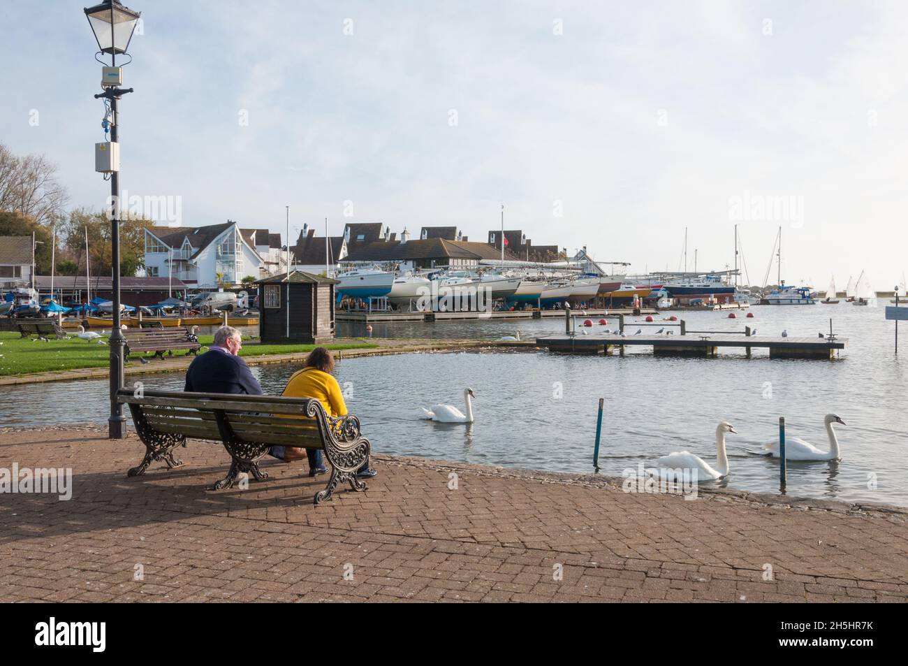 Una coppia seduta su una panchina godendosi una mattinata luminosa di sole a Town Quay, Christchurch, Dorset, Inghilterra, Regno Unito. Foto Stock